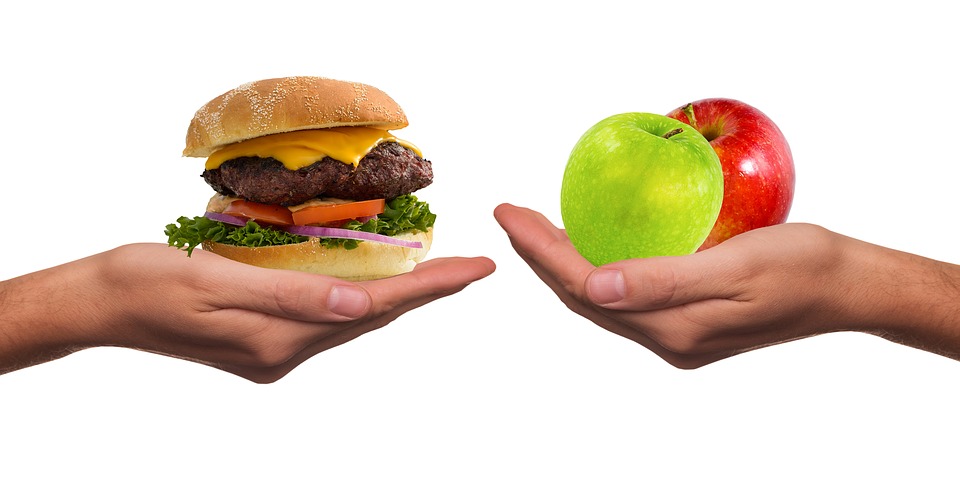 V jedné ruce hamburger, v druhé ruce jablka